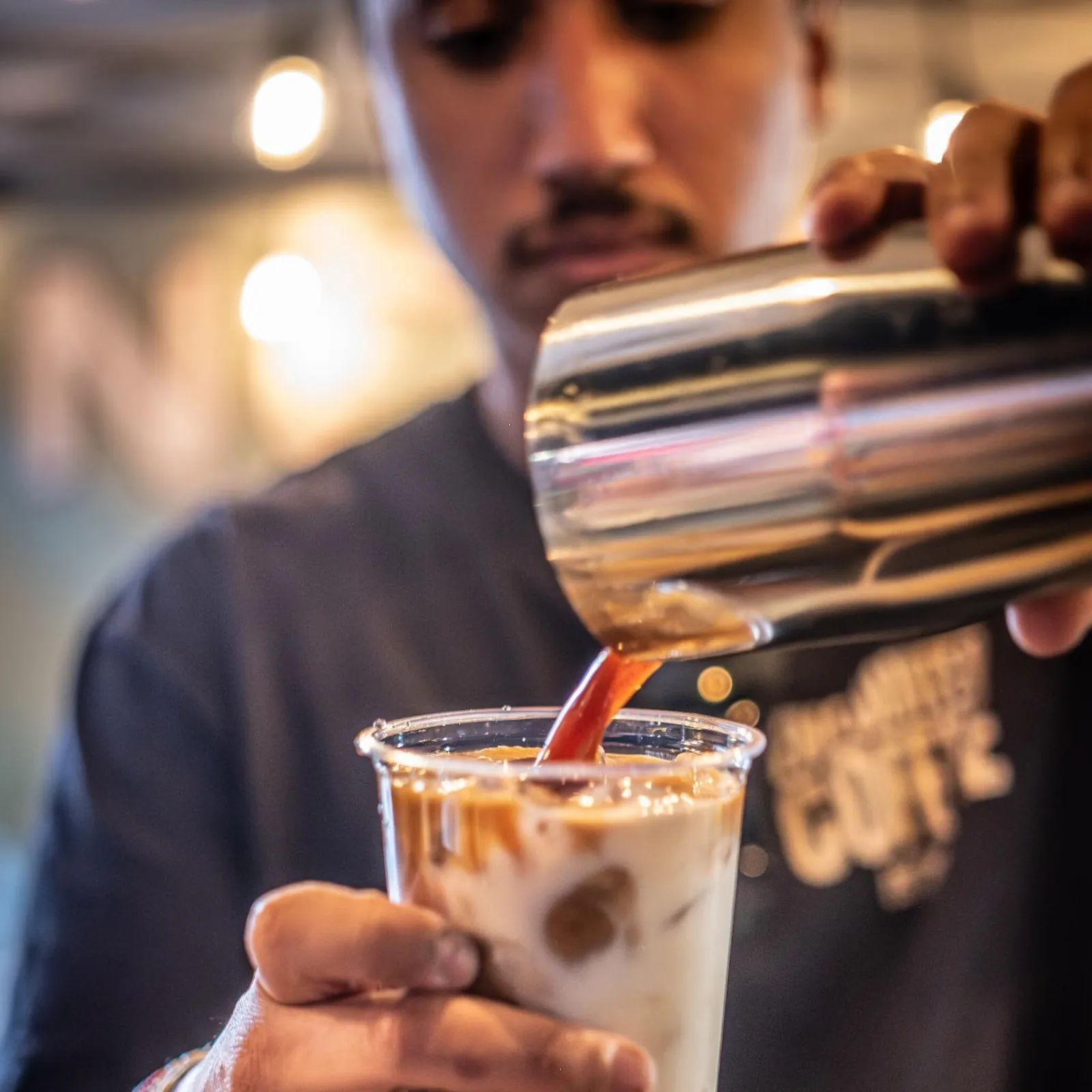 An Encounter Coffee barista pouring house-made caramel over an iced latte at an event
