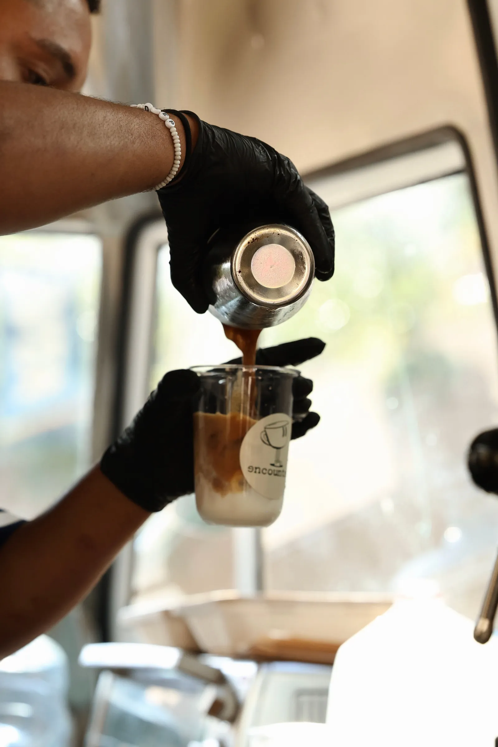 A barista pouring a fresh espresso shot over an iced latte in an Encounter Coffee branded cup inside the coffee bus