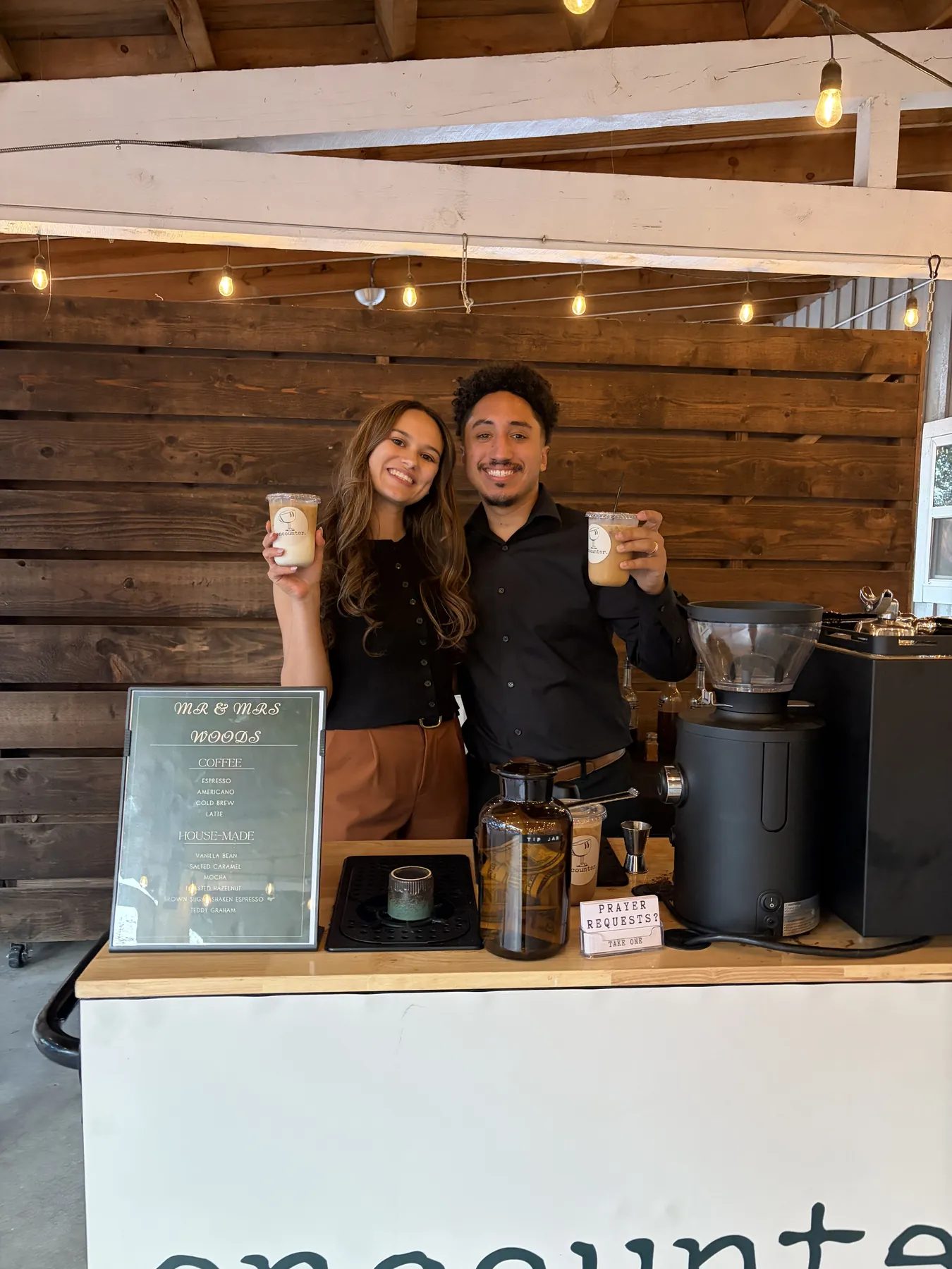 Aziel and Bri behind the Encounter Coffee cart with a custom wedding menu board printed for the couple