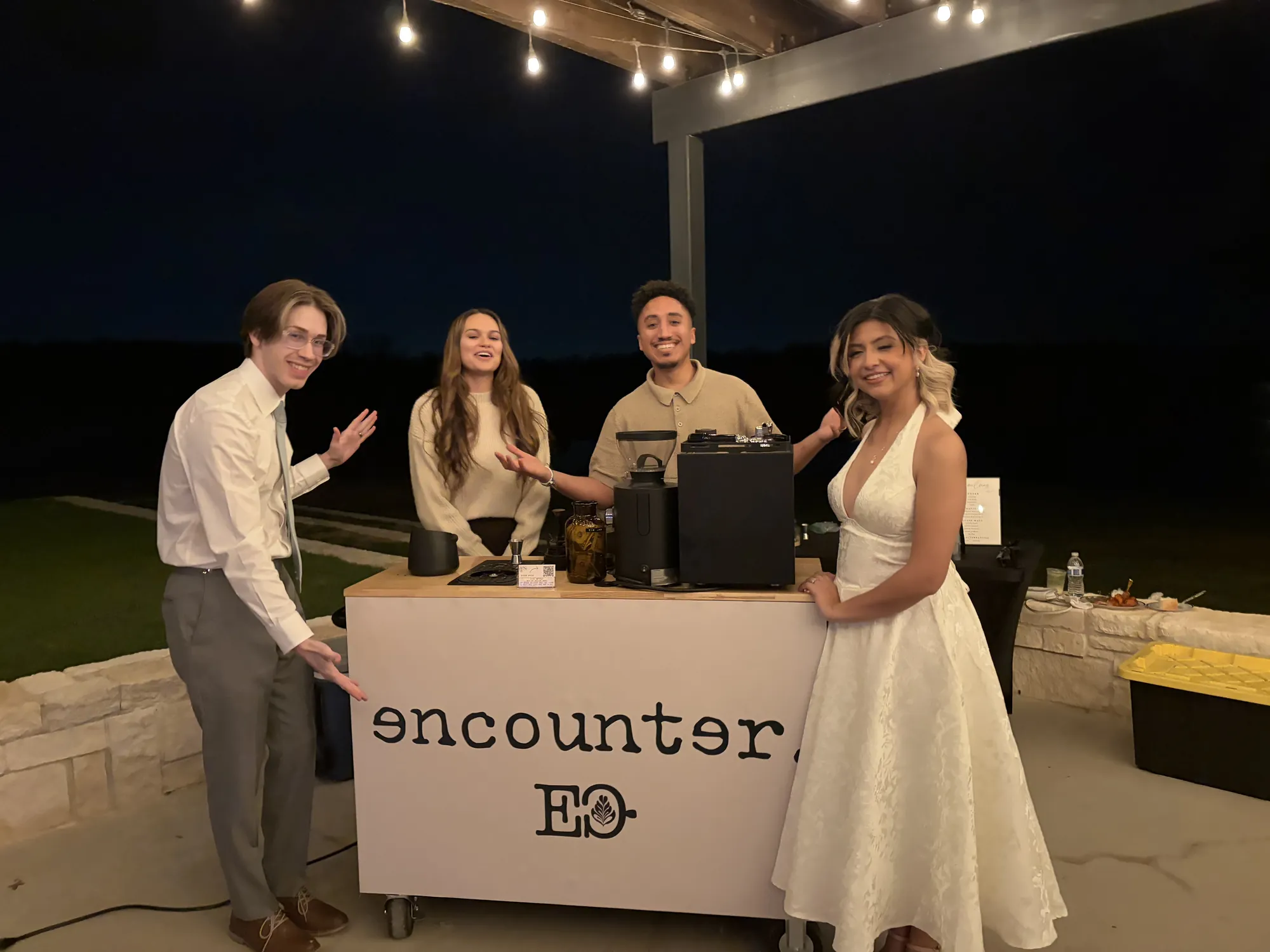 Encounter Coffee's mobile coffee cart set up under string lights at a Fort Worth wedding reception, with the bride and groom holding iced lattes
